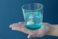 female hand holds transparent glass of water and effervescent tablet on a blue background.