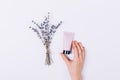 Female hand holds tube of cream next to bunch of lavender flowers