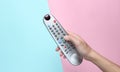 Female hand holds the TV remote on a pink blue pastel background. Top View. Royalty Free Stock Photo