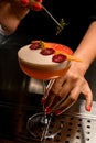 female hand holds tweezers with green twig and decorates glass with frothy drink