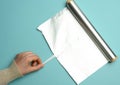 Female hand holds an unfolded roll of gray foil on a blue background Royalty Free Stock Photo