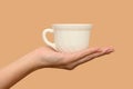 A female hand holds a white cup. Minimalism. Close-up. On a beige background.