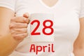 A female hand holds a white mug with inscription April 28. Business concept Royalty Free Stock Photo