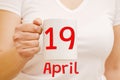 A female hand holds a white mug with inscription April 19. Business concept Royalty Free Stock Photo