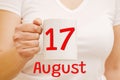 A female hand holds a white mug with the inscription 17 August. Business and holiday concept