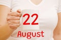 A female hand holds a white mug with the inscription 22 August. Business and holiday concept