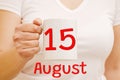 A female hand holds a white mug with the inscription 15 August. Business and holiday concept