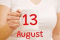 A female hand holds a white mug with the inscription 13 August. Business and holiday concept