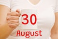 A female hand holds a white mug with the inscription 30 August. Business and holiday concept