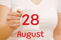 A female hand holds a white mug with the inscription 28 August. Business and holiday concept