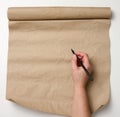 Female hand holds wooden pencil over brown paper roll on white table. Place to write text, list Royalty Free Stock Photo