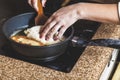 Female hand on inverted pie pan on electric stove