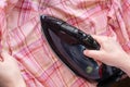 Female hand iron irons a checkered pink shirt. Housewife does housework. Top view. Royalty Free Stock Photo