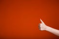 Female hand isolated on orange background shows thumb up in approval and like Royalty Free Stock Photo