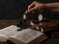 A female hand lights a candle on a table with old books, a quill pen and an antique pocket watch Royalty Free Stock Photo