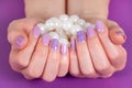 Female hand with a lilac color manicure holding pile of pearls isolated on purple background