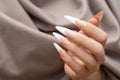 Female hand with long french nail design. Long french nail polish manicure. Woman hand on brown fabric background