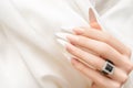 Female hand with long french nail design. Long french nail polish manicure. Woman hand on white fabric background