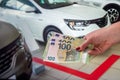 female hand with manicured red nails holds a large amount of euro banknotes near the car Royalty Free Stock Photo