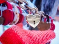 Female hand mitten holding golden padlock in form of heart outdoor in winter time.