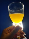 Female hand with nails holding a half glass of orange juice in front of white led light bulb with blue background beverage drink Royalty Free Stock Photo