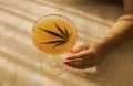 A female hand with a neat red manicure reaches for an elegant long-stemmed glass with a cocktail with cannabis leaves. A delicious