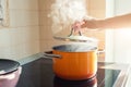 Female hand open lid of enamel steel cooking pan on electric hob with boiling water or soup and scenic vapor steam