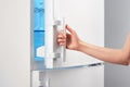 Female hand opening white refrigerator door on gray Royalty Free Stock Photo