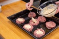 Female hand overlays stuffing theminced meat or meatballs laying on a black baking tray. Process of cooking