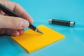 A female hand with a pen writes on a blank orange sticker. Blue background. Copy of space. close-up. Place for text. Royalty Free Stock Photo