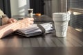 Female hand with pen writing smth in diary. Woman sitting at table with collapsible cup in cafe with sunshine and taking Royalty Free Stock Photo