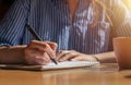 Female hand with pen writing smth in planner and taking notes on notepad on wood desk, closeup Royalty Free Stock Photo