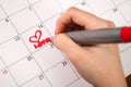 Female hand with pencil drawing heart and word love in calendar for Valentines day Royalty Free Stock Photo