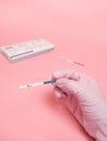 Female hand in a pink medical glove holding positive pregnancy test isolated on pink background. The abbreviation HCG on