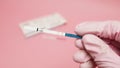 Female hand in a pink medical glove holding positive pregnancy test isolated on pink background. The abbreviation HCG on