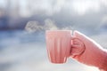 Female hand in pink mittens holding cup with hot tea or coffee. Close up