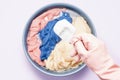 Female hand in a pink rubber glove holds scoop with washing powder on a late basin with soaked laundry on lilac Royalty Free Stock Photo