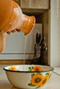 Female hand pouring ceramic ewer oil into a metal bowl. painted in white enamel, a brown earthenware jug close-up vertical. Royalty Free Stock Photo