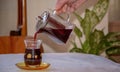 Female hand pouring hibiscus tea into classic turkish tea cup, closeup