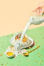 Female hand pouring milk into bowl with muesli, cereal with berries against pastel background. Overflow of milk Royalty Free Stock Photo