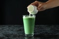 Female hand pouring milk into a glass of matcha latte against black background Royalty Free Stock Photo