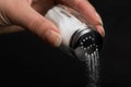 Female hand pouring salt from salt shaker on black Royalty Free Stock Photo