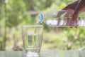 Female hand pouring water from bottle to glass on nature Royalty Free Stock Photo