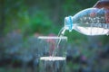 Female hand pouring water from bottle to glass on nature Royalty Free Stock Photo