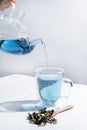 A female hand pours blue tea from a glass teapot into a mug. Butterfly pea flower tea is brewed in teapot and served into a Royalty Free Stock Photo