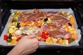 Female hand pours sauce for marinating pieces of pork on finely chopped and seasoned vegetables on a baking sheet for cooking in Royalty Free Stock Photo