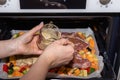 Female hand pours sauce for marinating pieces of pork on finely chopped and seasoned vegetables on a baking sheet for cooking in Royalty Free Stock Photo