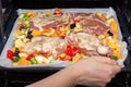Female hand pours sauce for marinating pieces of pork on finely chopped and seasoned vegetables on a baking sheet for cooking in Royalty Free Stock Photo