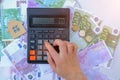 female hand presses buttons on the calculator, against the background of euro banknotes and coins. Small wooden toy Royalty Free Stock Photo