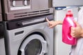 Female hand presses start button on washing machine, holding detergent in hands Royalty Free Stock Photo